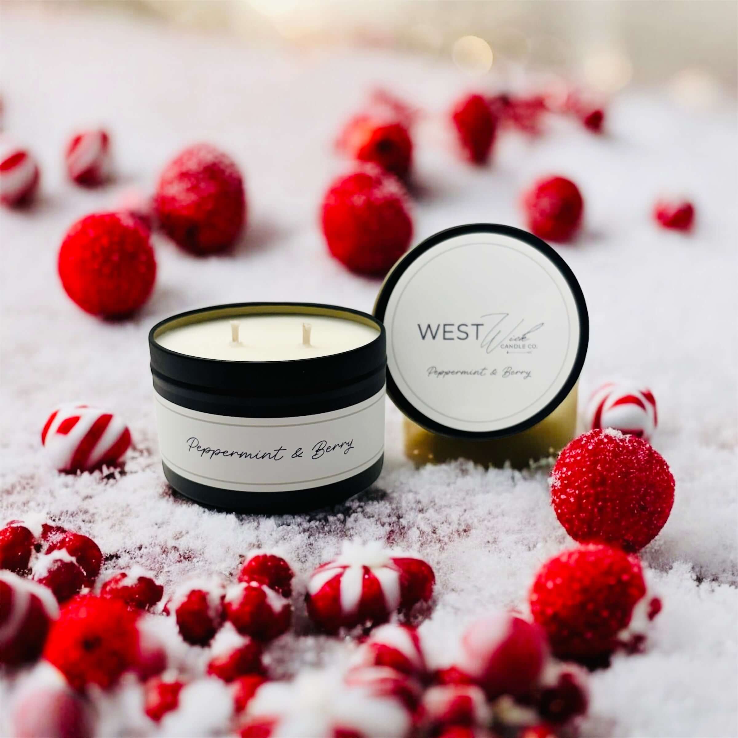 Peppermint &amp; Berry Black Luxe Candle surrounded by festive red berries and peppermint candies on snow.