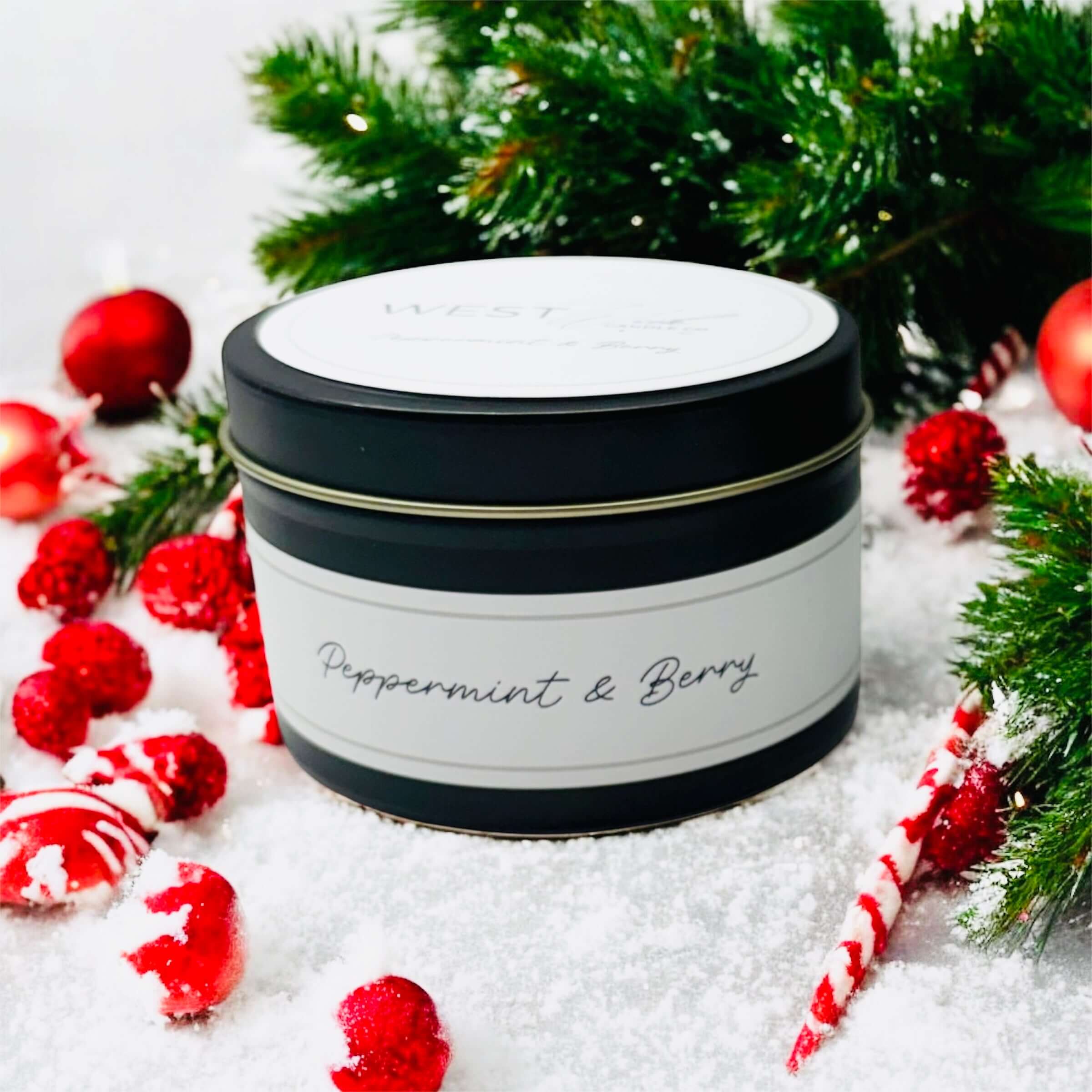Peppermint &amp; Berry Black Luxe Candle surrounded by festive decorations and greenery.