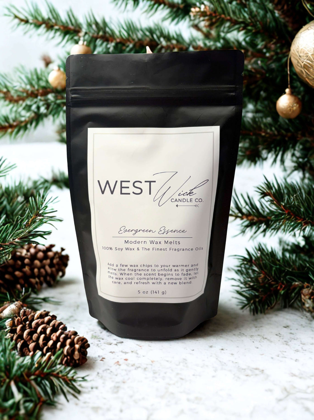 Evergreen Essence Wax Melts by WEST WILD Candle Co in a black pouch with festive pine branches.